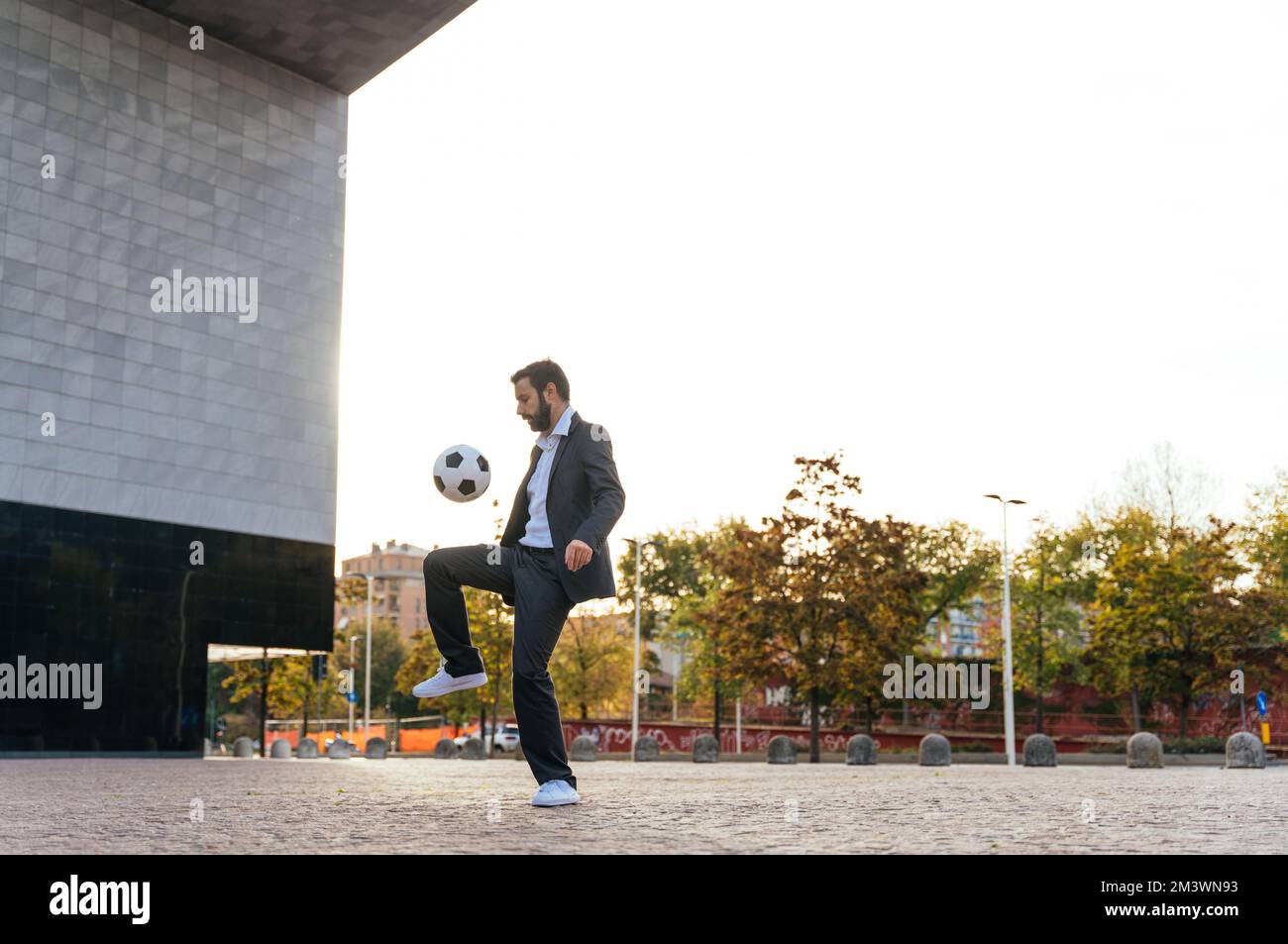 Bild eines Geschäftsmanns und Freispielers, der mit dem Ball auf der Straße Tricks macht. Konzept über Sport- und Geschäftsleute Stockfoto
