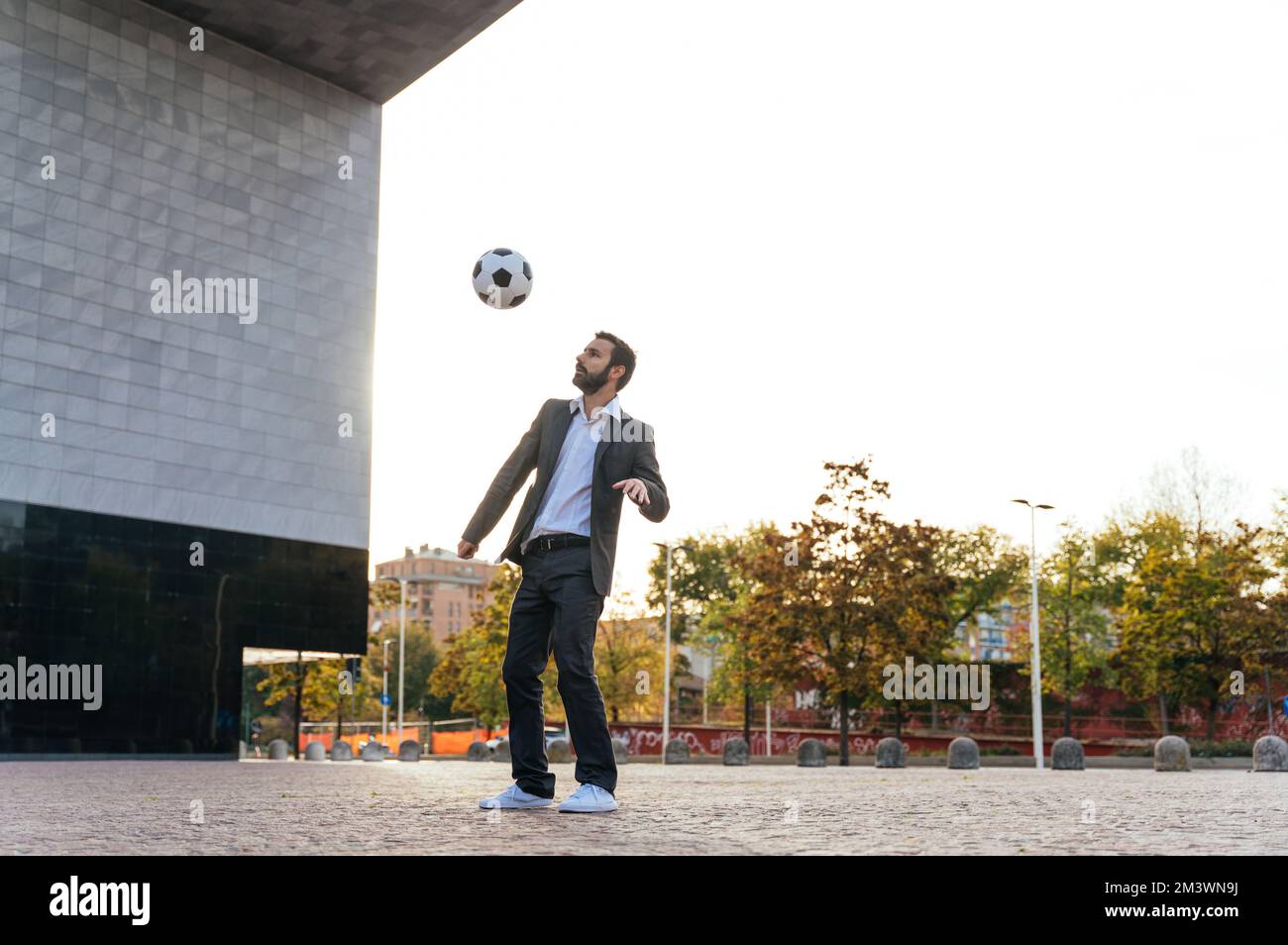 Bild eines Geschäftsmanns und Freispielers, der mit dem Ball auf der Straße Tricks macht. Konzept über Sport- und Geschäftsleute Stockfoto