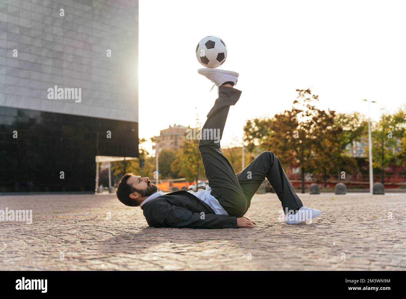 Bild eines Geschäftsmanns und Freispielers, der mit dem Ball auf der Straße Tricks macht. Konzept über Sport- und Geschäftsleute Stockfoto