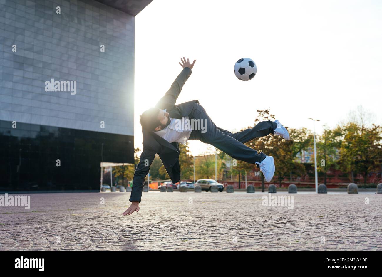 Bild eines Geschäftsmanns und Freispielers, der mit dem Ball auf der Straße Tricks macht. Konzept über Sport- und Geschäftsleute Stockfoto