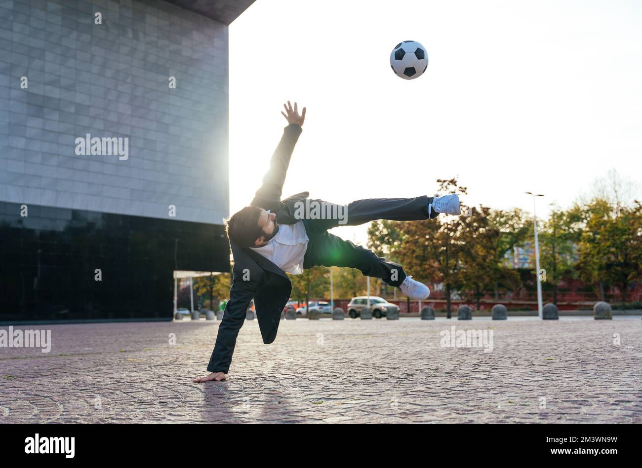 Bild eines Geschäftsmanns und Freispielers, der mit dem Ball auf der Straße Tricks macht. Konzept über Sport- und Geschäftsleute Stockfoto