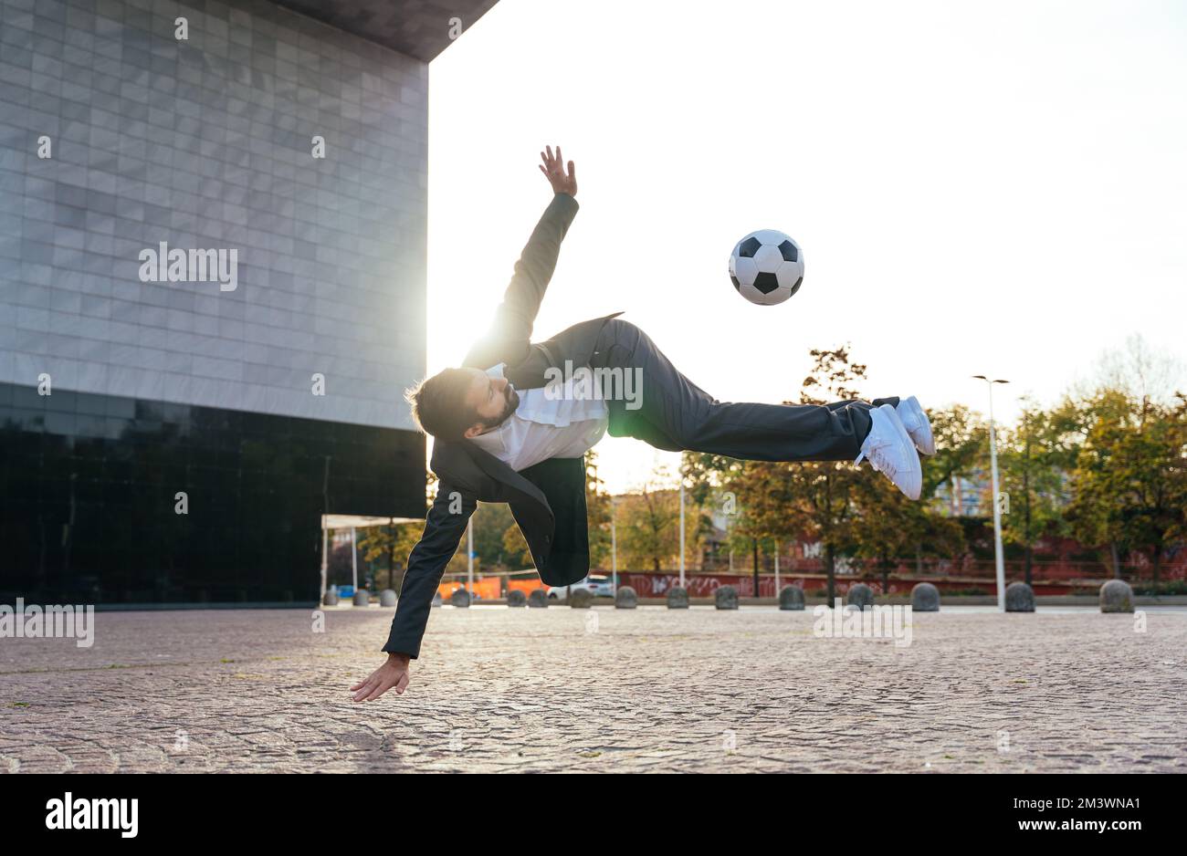 Bild eines Geschäftsmanns und Freispielers, der mit dem Ball auf der Straße Tricks macht. Konzept über Sport- und Geschäftsleute Stockfoto