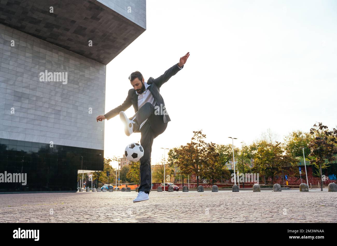 Bild eines Geschäftsmanns und Freispielers, der mit dem Ball auf der Straße Tricks macht. Konzept über Sport- und Geschäftsleute Stockfoto