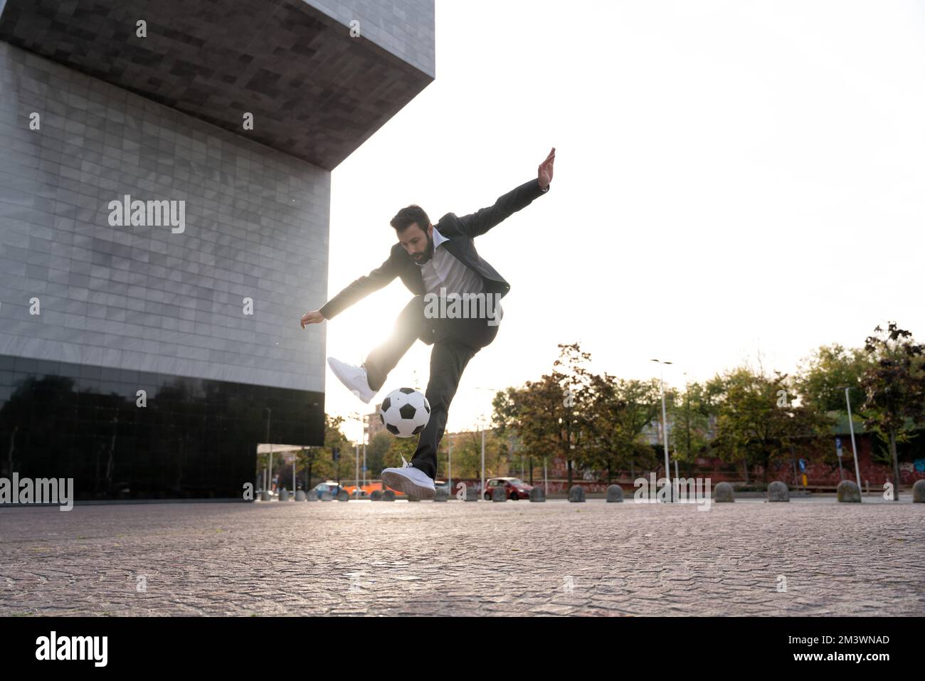 Bild eines Geschäftsmanns und Freispielers, der mit dem Ball auf der Straße Tricks macht. Konzept über Sport- und Geschäftsleute Stockfoto