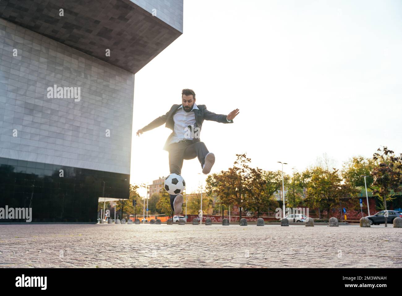 Bild eines Geschäftsmanns und Freispielers, der mit dem Ball auf der Straße Tricks macht. Konzept über Sport- und Geschäftsleute Stockfoto
