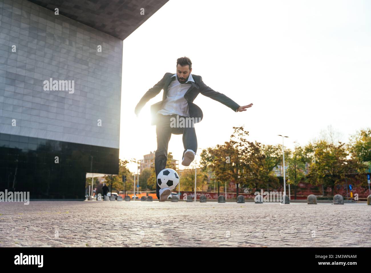 Bild eines Geschäftsmanns und Freispielers, der mit dem Ball auf der Straße Tricks macht. Konzept über Sport- und Geschäftsleute Stockfoto