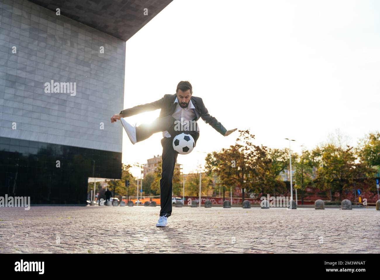 Bild eines Geschäftsmanns und Freispielers, der mit dem Ball auf der Straße Tricks macht. Konzept über Sport- und Geschäftsleute Stockfoto