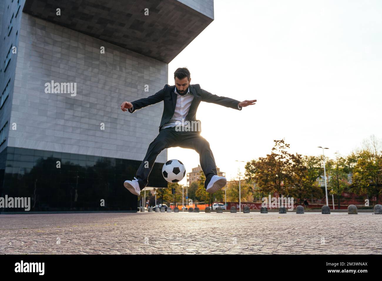 Bild eines Geschäftsmanns und Freispielers, der mit dem Ball auf der Straße Tricks macht. Konzept über Sport- und Geschäftsleute Stockfoto