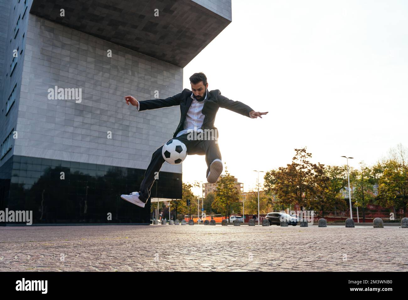 Bild eines Geschäftsmanns und Freispielers, der mit dem Ball auf der Straße Tricks macht. Konzept über Sport- und Geschäftsleute Stockfoto