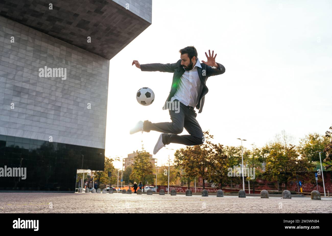 Bild eines Geschäftsmanns und Freispielers, der mit dem Ball auf der Straße Tricks macht. Konzept über Sport- und Geschäftsleute Stockfoto