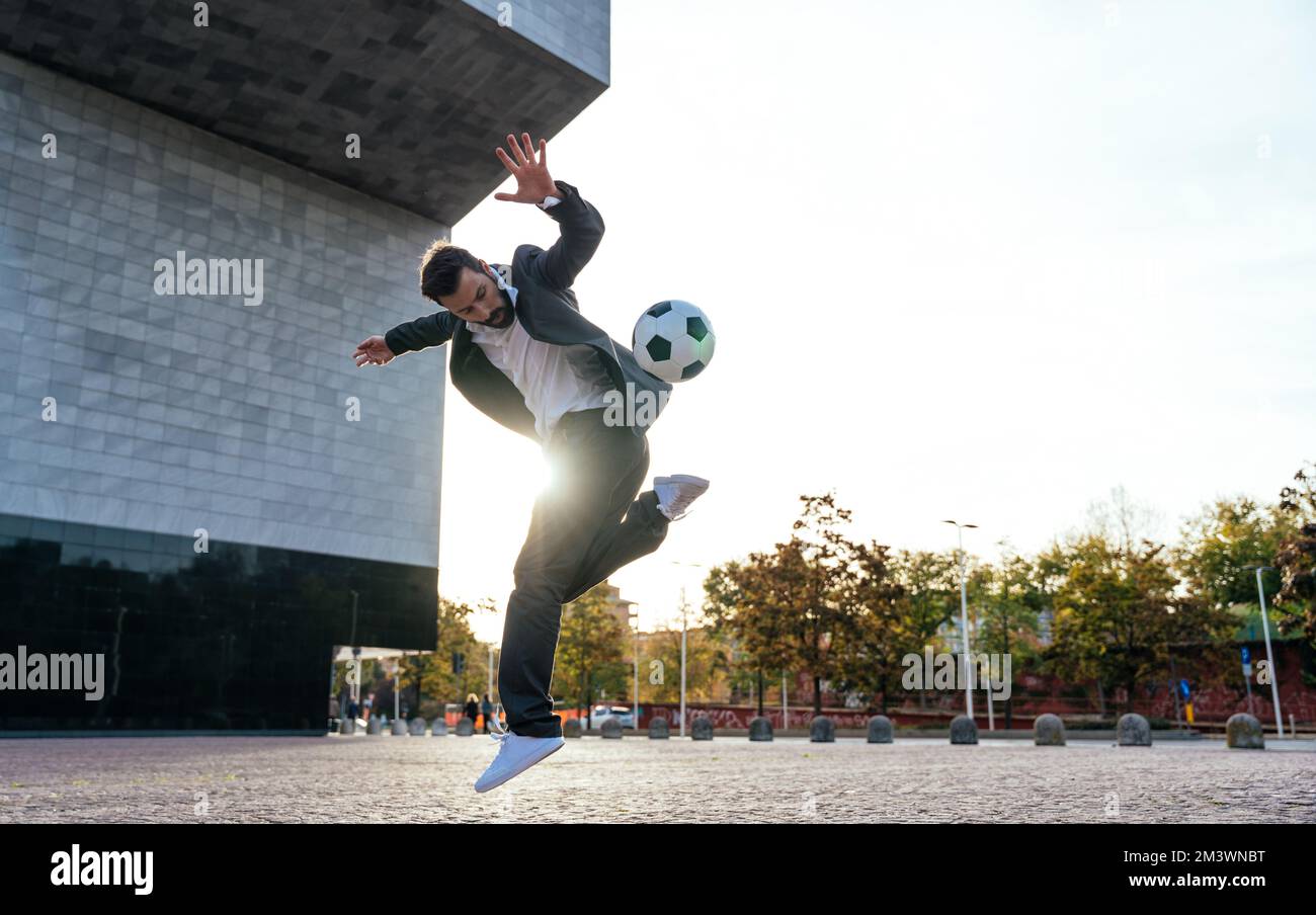 Bild eines Geschäftsmanns und Freispielers, der mit dem Ball auf der Straße Tricks macht. Konzept über Sport- und Geschäftsleute Stockfoto