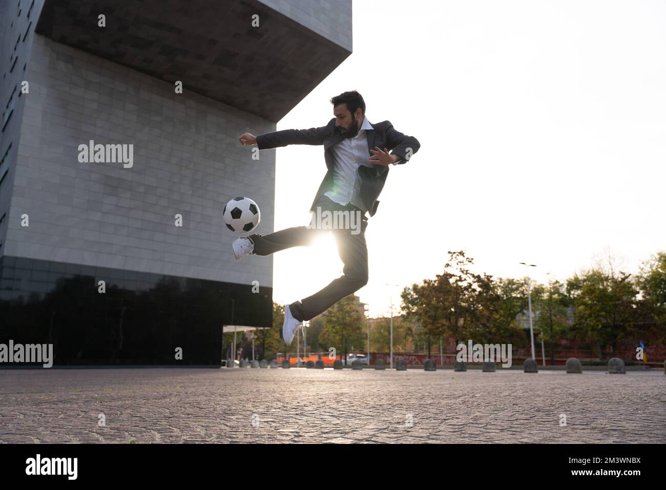Bild eines Geschäftsmanns und Freispielers, der mit dem Ball auf der Straße Tricks macht. Konzept über Sport- und Geschäftsleute Stockfoto
