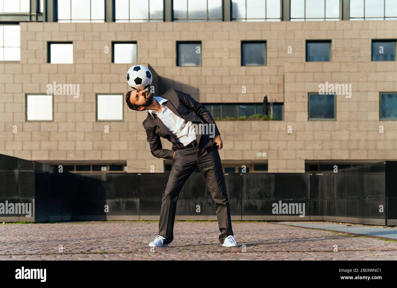 Bild eines Geschäftsmanns und Freispielers, der mit dem Ball auf der Straße Tricks macht. Konzept über Sport- und Geschäftsleute Stockfoto