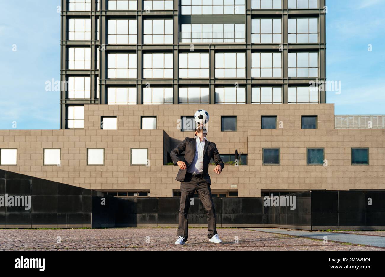 Bild eines Geschäftsmanns und Freispielers, der mit dem Ball auf der Straße Tricks macht. Konzept über Sport- und Geschäftsleute Stockfoto