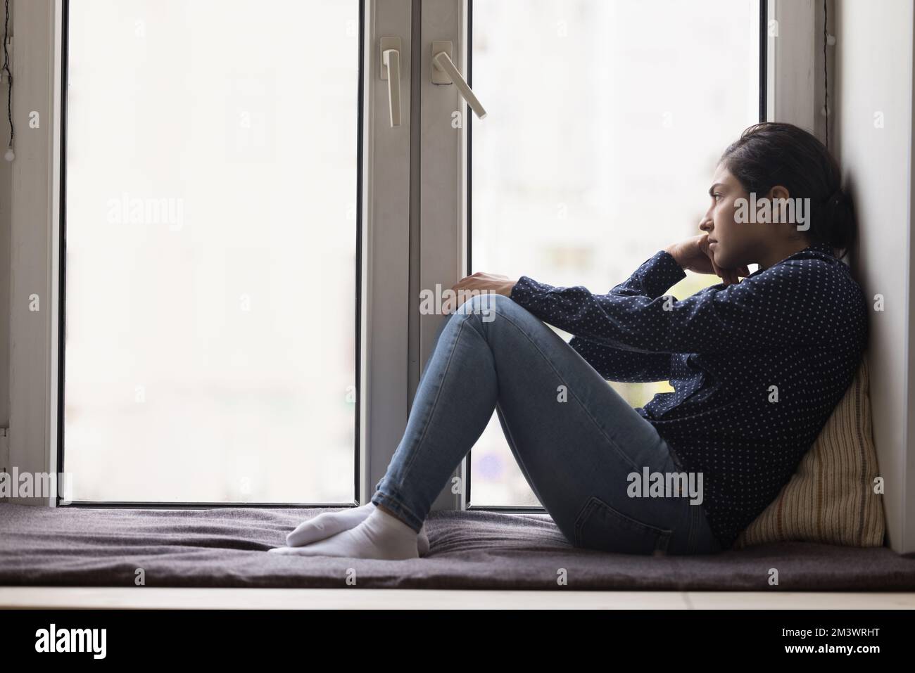 Unglückliche, einsame, junge Indianerin, die auf einer Fensterbank sitzt Stockfoto