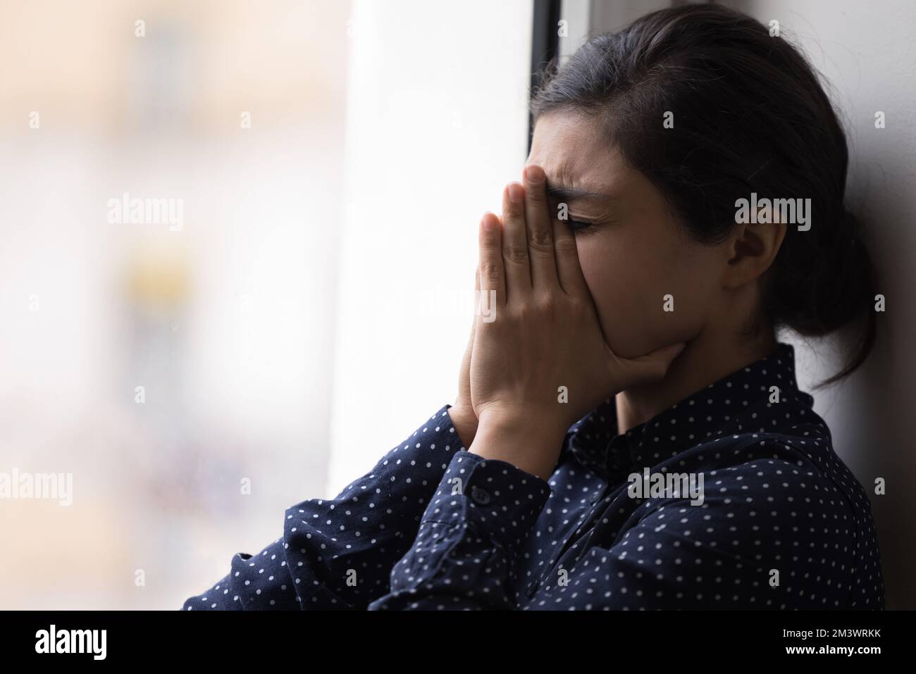 Frustrierte, unglückliche, junge Indianerin, die am Fenster weint Stockfoto