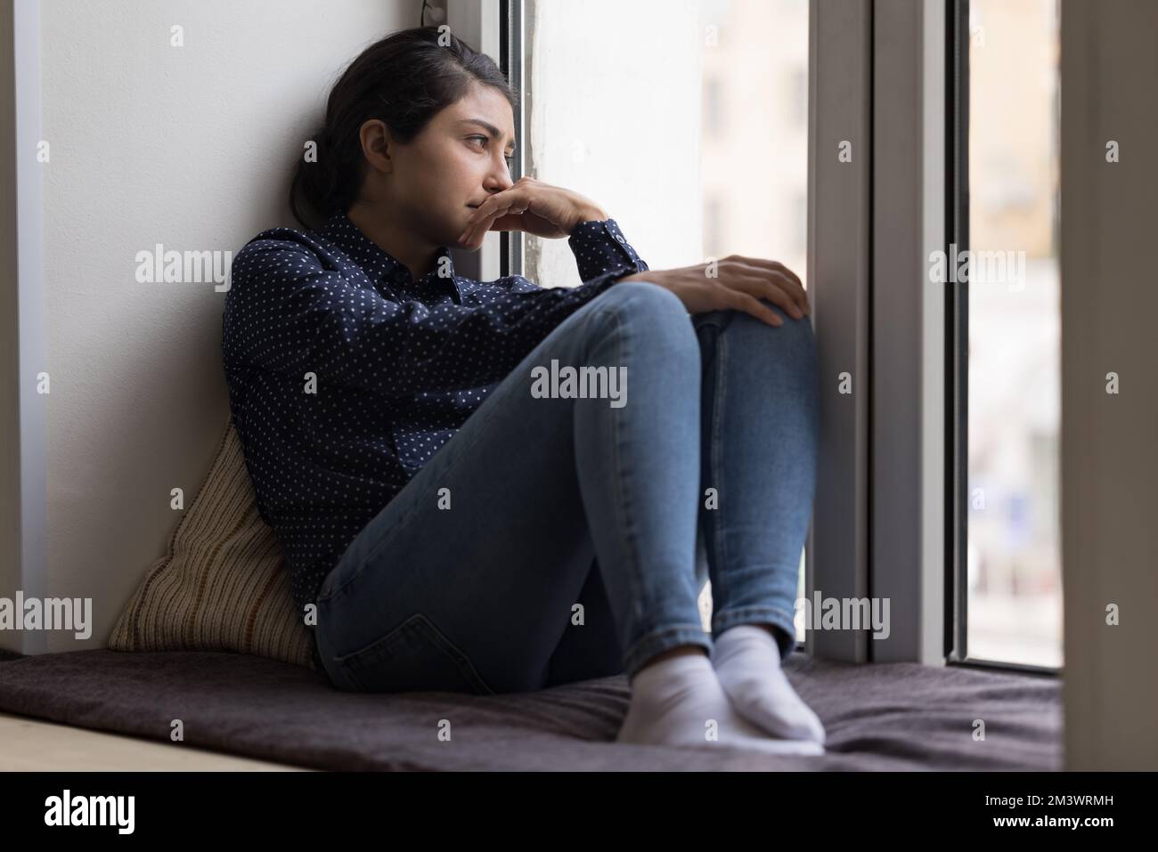 Deprimierte, aufgewühlte Indianerin, die auf einer weichen Fensterbank ruht Stockfoto