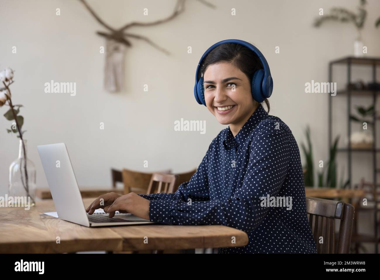 Fröhliche, wunderschöne Studentin aus Indien, die kabellose Kopfhörer mit einem Laptop trägt Stockfoto