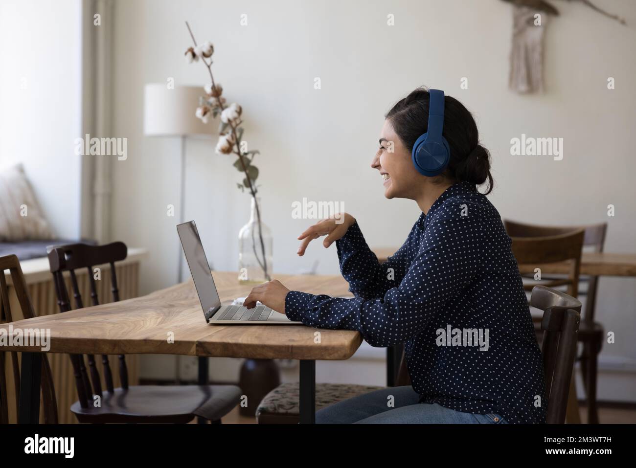 Fröhliche indische Schülerin mit Kopfhörern, die über den Laptop lacht Stockfoto