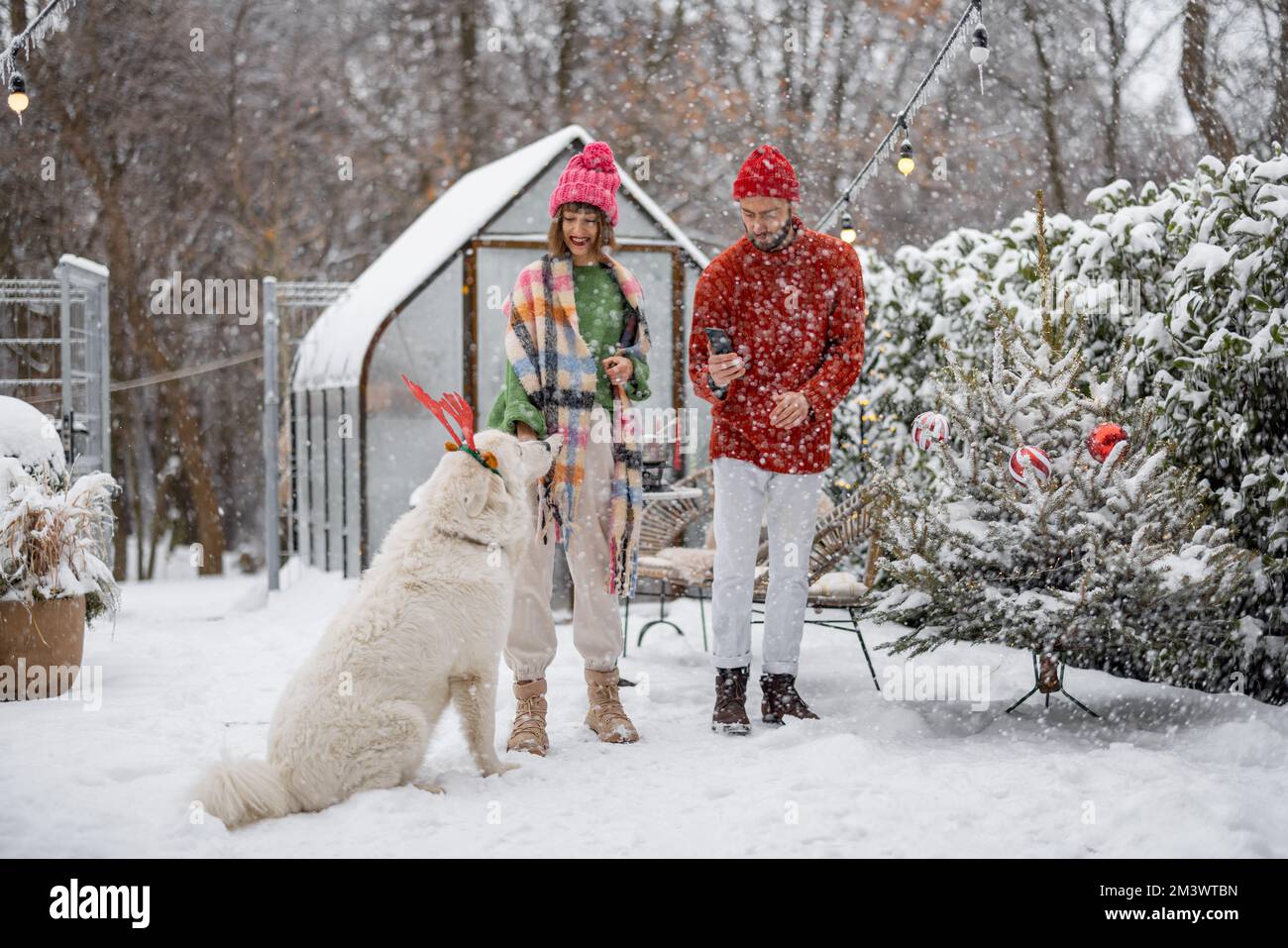 Junge Familie mit einem Hund im verschneiten Hinterhof während der Winterferien Stockfoto