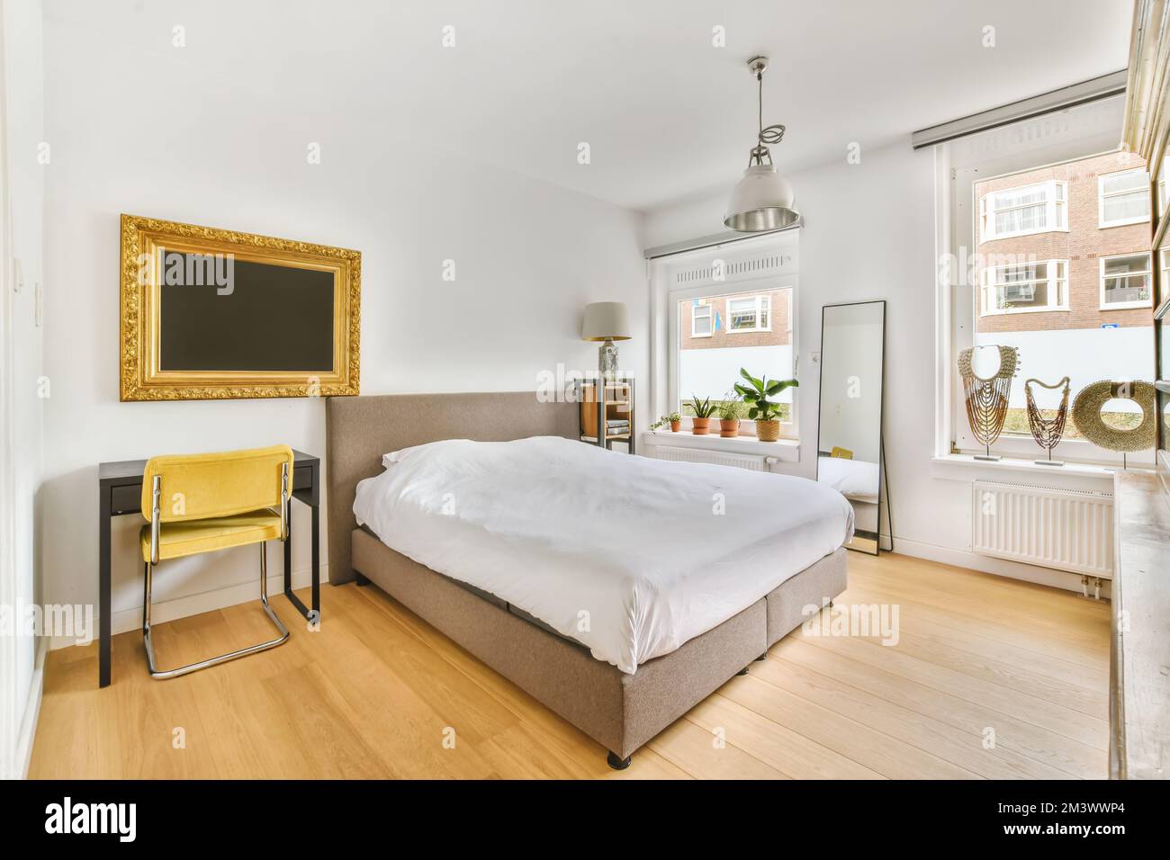 Ein Schlafzimmer mit weißen Wänden und Holzfußboden in der Mitte des Zimmers, es gibt einen fernseher an der Wand Stockfoto