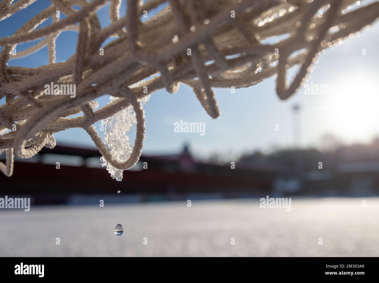 Nahaufnahme von schmelzendem Eis auf dem Tornetz auf dem Fußballfeld mit Schnee bedeckt. Stockfoto