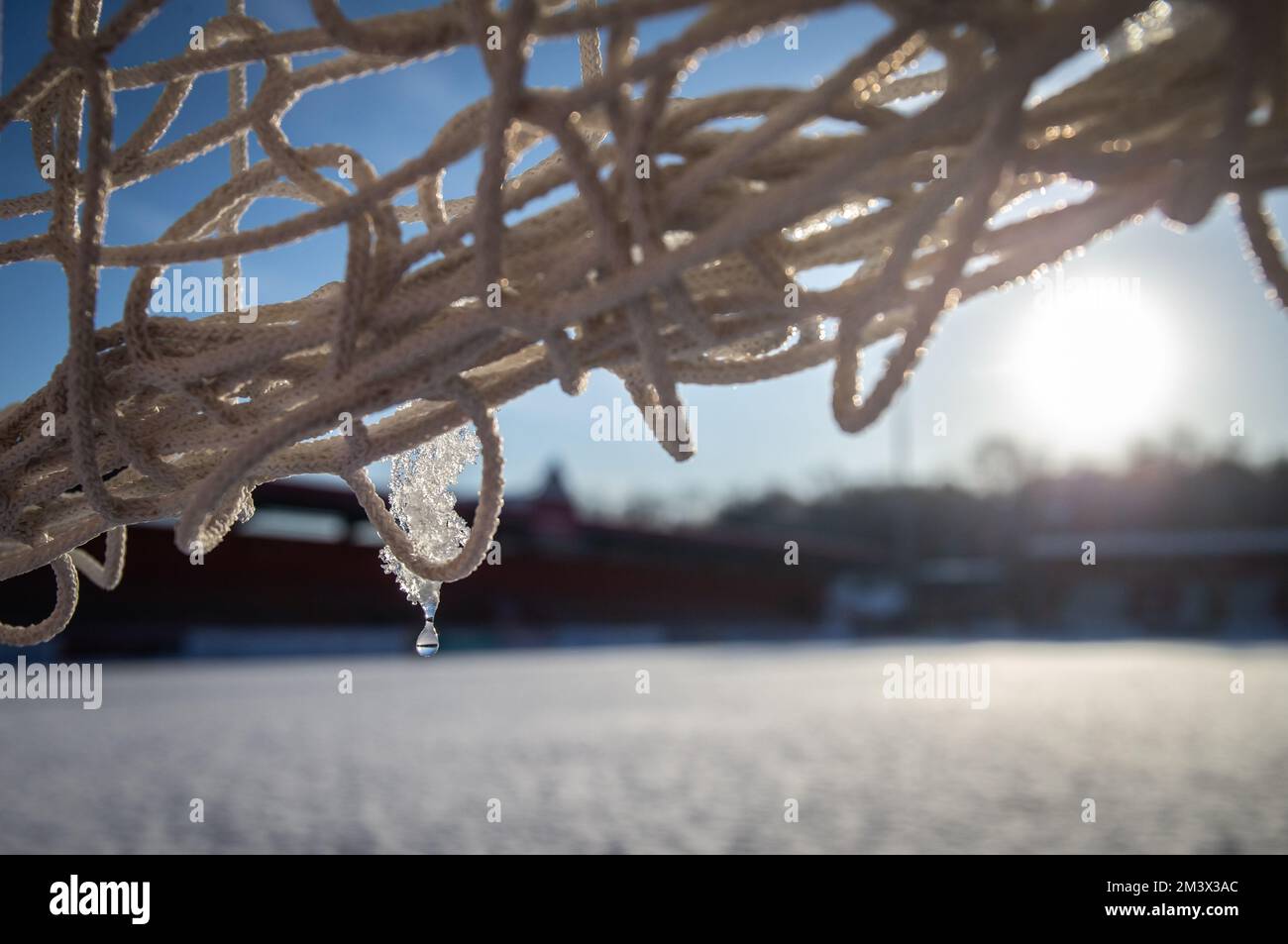 Nahaufnahme von schmelzendem Eis auf dem Tornetz auf dem Fußballfeld mit Schnee bedeckt. Stockfoto