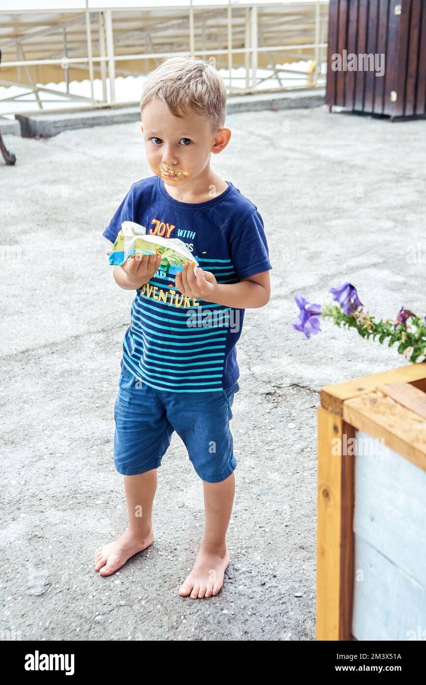 Der Vorschuljunge bekommt ein dreckiges Gesicht und isst Lieblingseis auf der Sea Resort Street. Der blonde Kerl verbringt gern Sommerferien und ruht sich aus Stockfoto