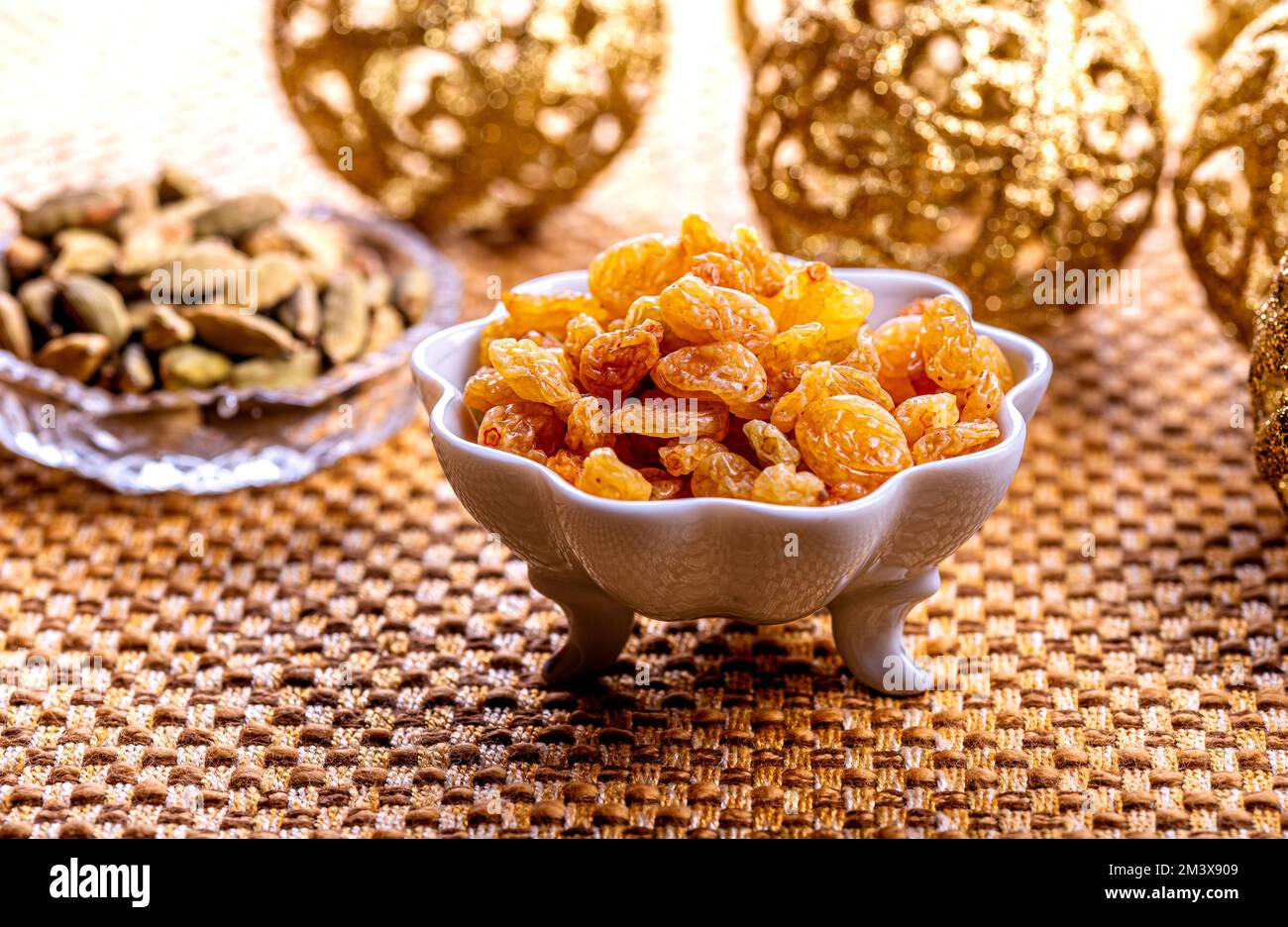 Gelbe goldene Rosinen in weißer Keramikschüssel auf goldenem Hintergrund. Stockfoto