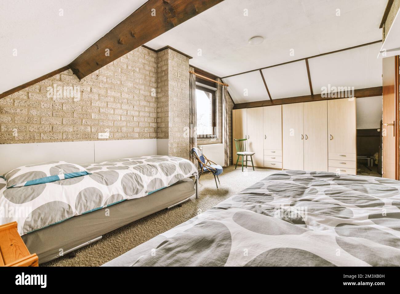 Ein Schlafzimmer mit einem Bett, Kommoden und fernseher in der Ecke auf der linken Seite des Zimmers ist eine alte Backsteinwand Stockfoto