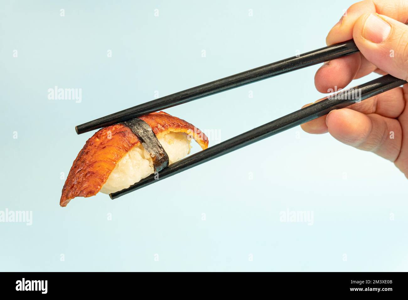 Sushi Nigiri mit Aal Unagi auf blauem Hintergrund. Traditionelle japanische Küche. Sushi-Nahaufnahme. Sushi auf Stäbchen in der Hand Nahaufnahme. Stockfoto
