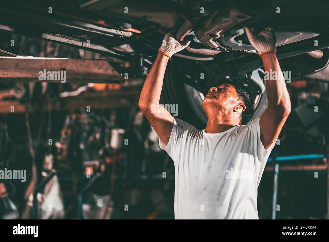 Garagenarbeiter, asiatisches Mechaniker-Team, das Auto-Service-Reparatur repariert, Austausch unter Hebebühne Stockfoto