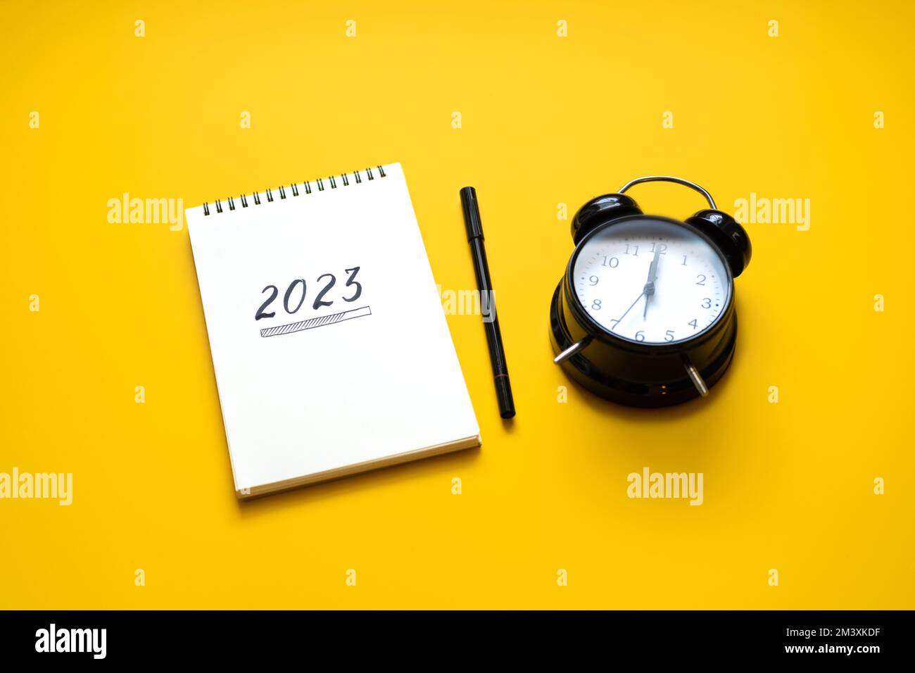 Neujahrsauflösung, Zielsetzung für das 2023. Jahr, Text 2023 wird in offenen Notizblock geladen und Wecker auf gelbem Schreibtischhintergrund. Ein neues Leben beginnen Stockfoto