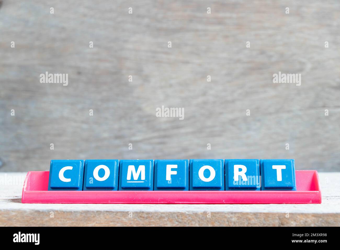 Buchstabenziegel mit Wort Comfort in rotem Regal auf Holzhintergrund Stockfoto