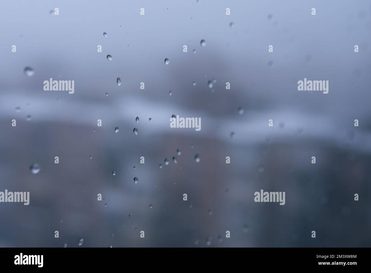 Die unglückliche Szene, nebiges Glasfenster mit Regentropfen. Selektiver Fokus auf das Foto. Verschwommener Hintergrund mit Häusern. Stadtlandschaft. Depression und Traurigkeit. Stockfoto