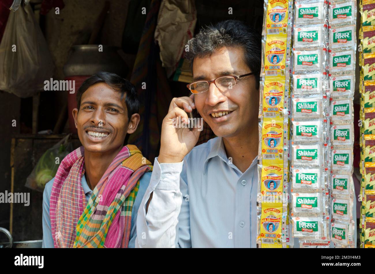 Ein Mann benutzt ein Handy, ein anderer lächelt hinten. Kalkutta, Indien Stockfoto