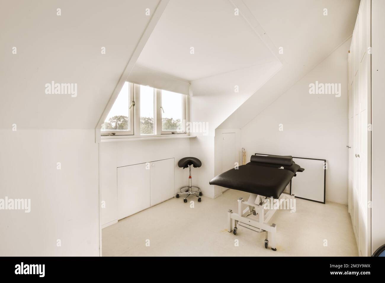 Ein weißes Zimmer mit einem schwarzen Stuhl und einem offenen Fenster im Zimmer ist sehr sauber, aber es ist nicht länger als Stockfoto