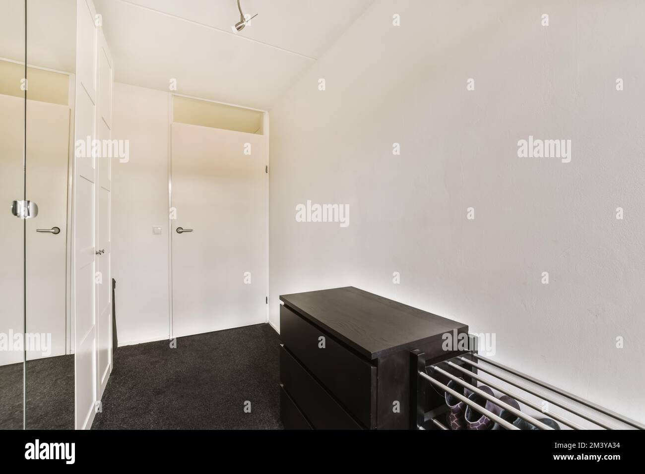 Ein Zimmer mit weißen Wänden und schwarzem Fußboden, einschließlich eines großen Spiegels an der Wand neben der Schranktür Stockfoto