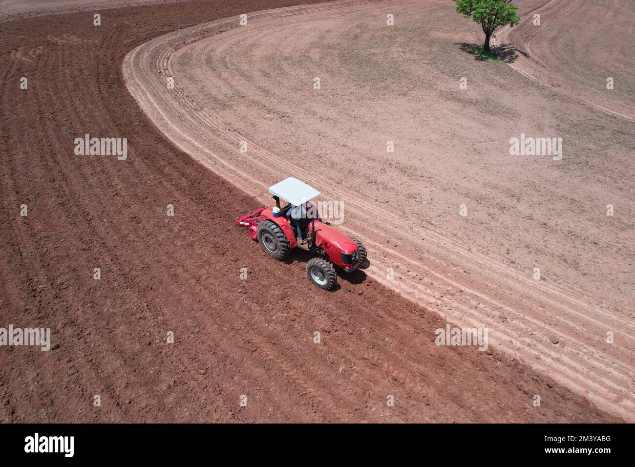 Eine Luftaufnahme eines kleinen roten Traktors, der ein großes Feld pflügt Stockfoto