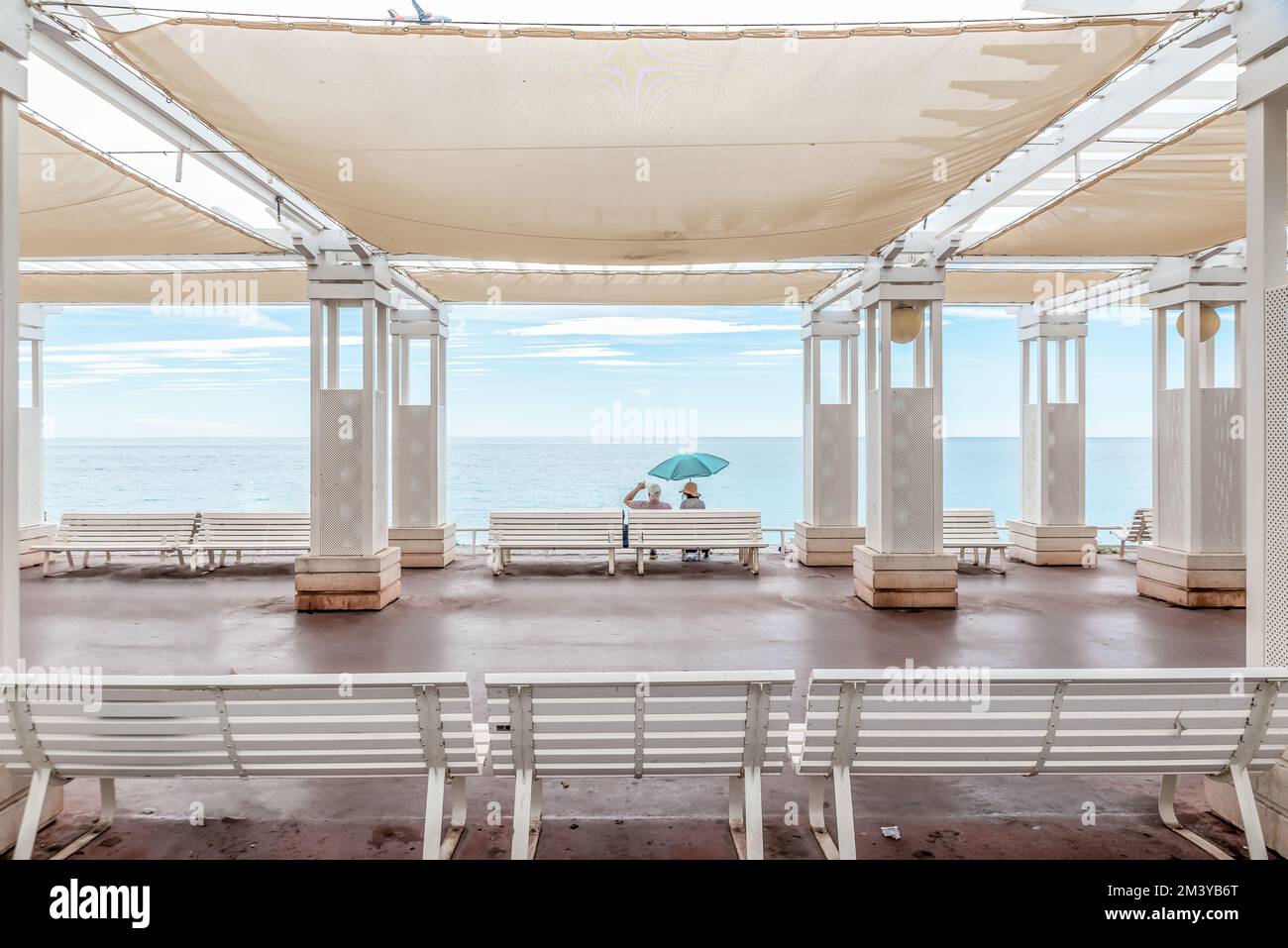 Ein Paar, das auf einer weißen Bank unter einem Pavillon am Strand sitzt Stockfoto