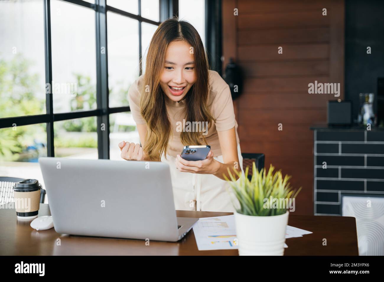 Aufgeregtes weibliches Lächeln bekam gute Nachrichten auf dem Smartphone, während ich am Computer arbeitete Stockfoto