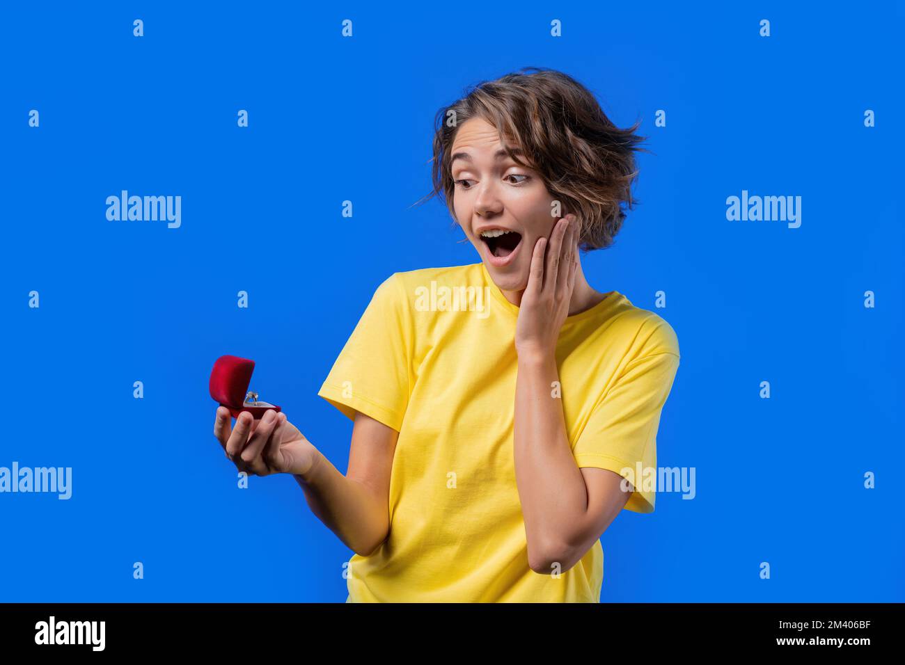 Pretty Woman bekam Schmuckkiste mit Diamantring auf blauem Hintergrund. Eine überraschte lächelnde Dame, die glücklich ist, ihre Verlobte zu sein Stockfoto