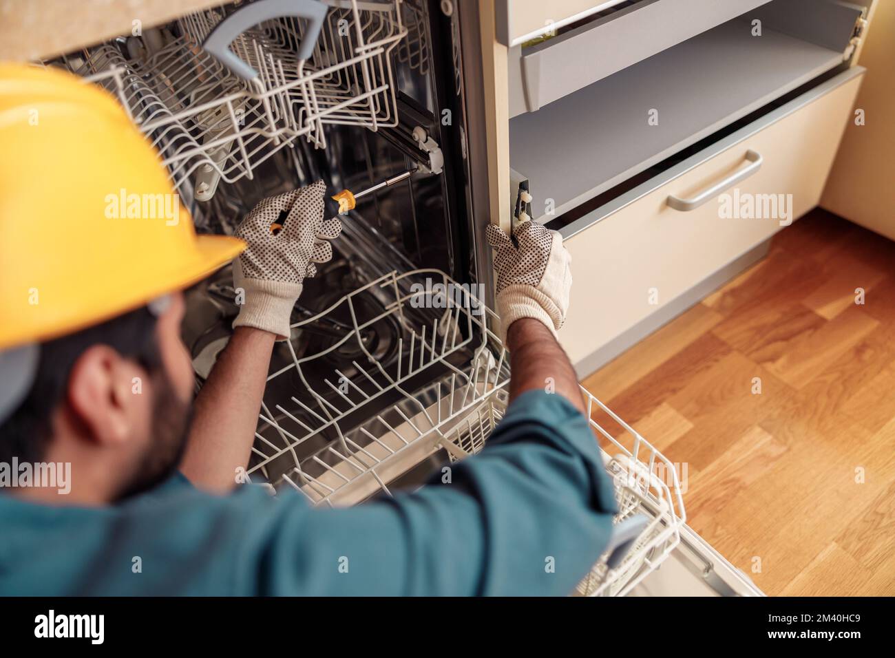 Nahaufnahme eines Handwerkers in Spezialkleidung, der Geschirrspüler in der modernen Küche repariert Stockfoto
