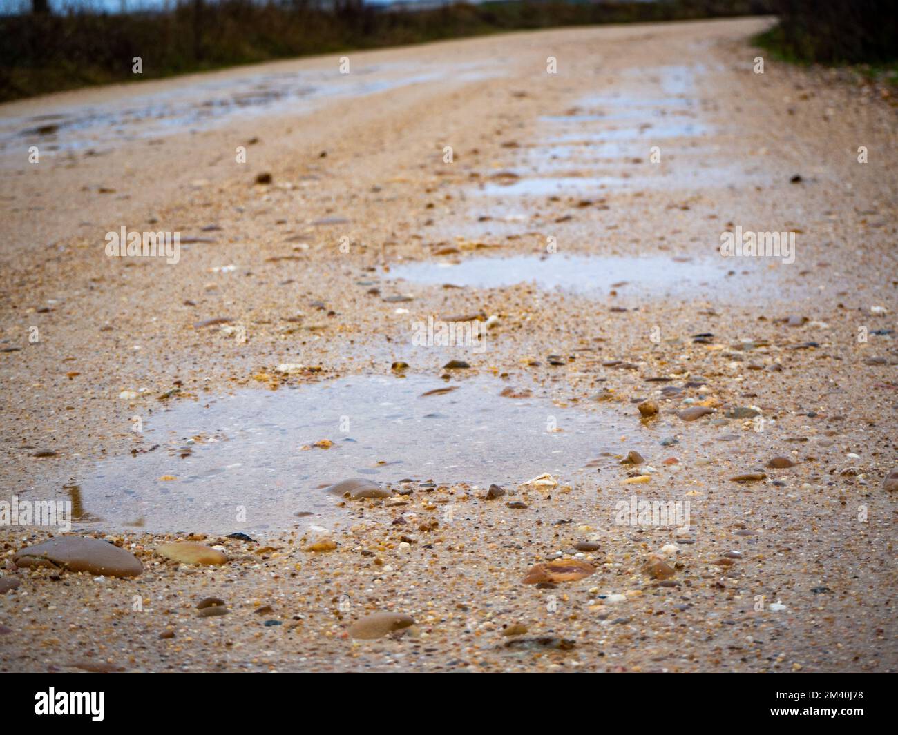 Mit Wasser gefüllte Schlaglöcher auf einer sandigen Straße nach dem Regen Stockfoto