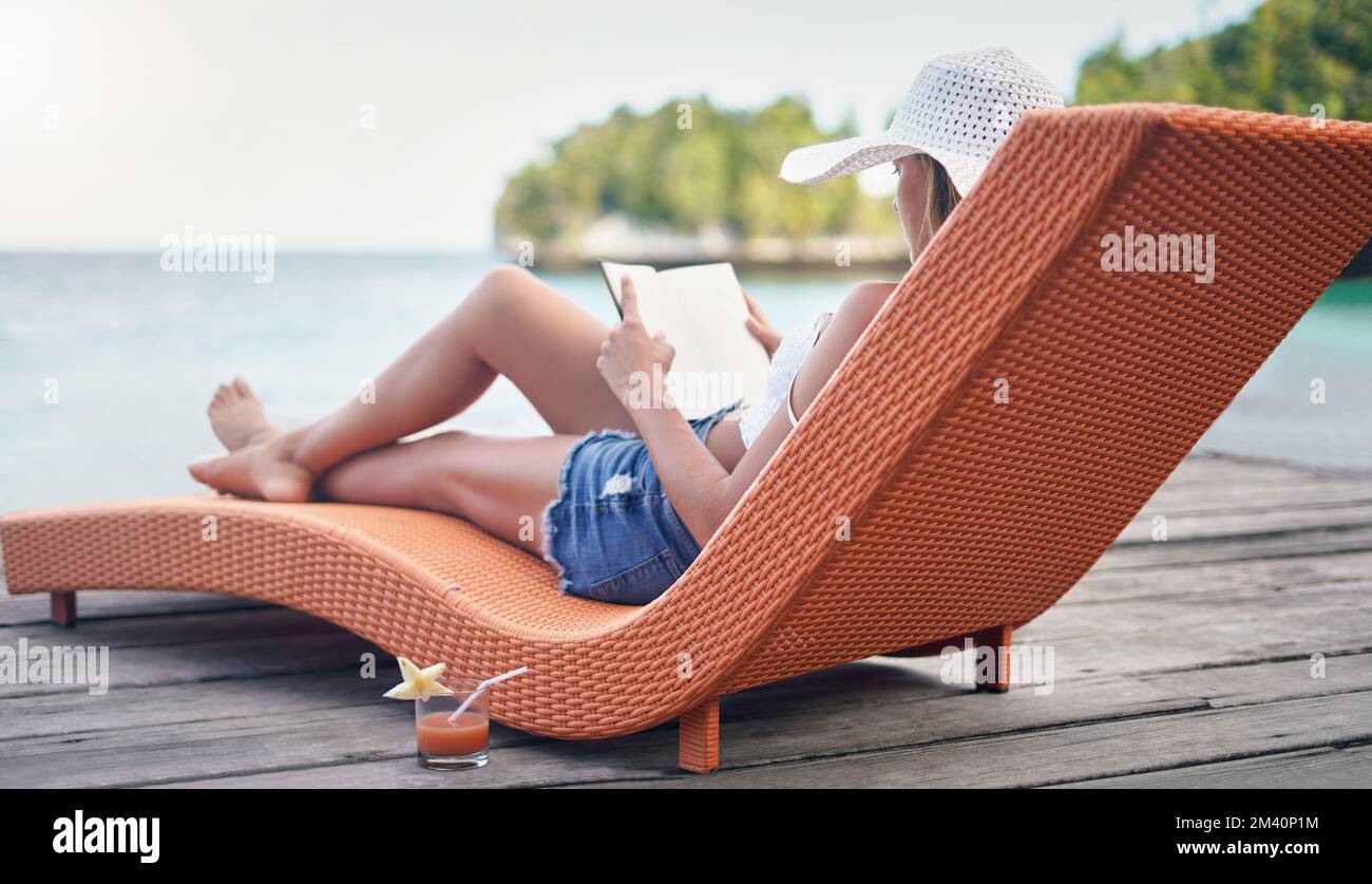 Das ist mein glücklicher Ort. Aufnahme einer attraktiven jungen Frau, die auf einer Sonnenliege sitzt und während des Urlaubs ein Buch liest. Stockfoto