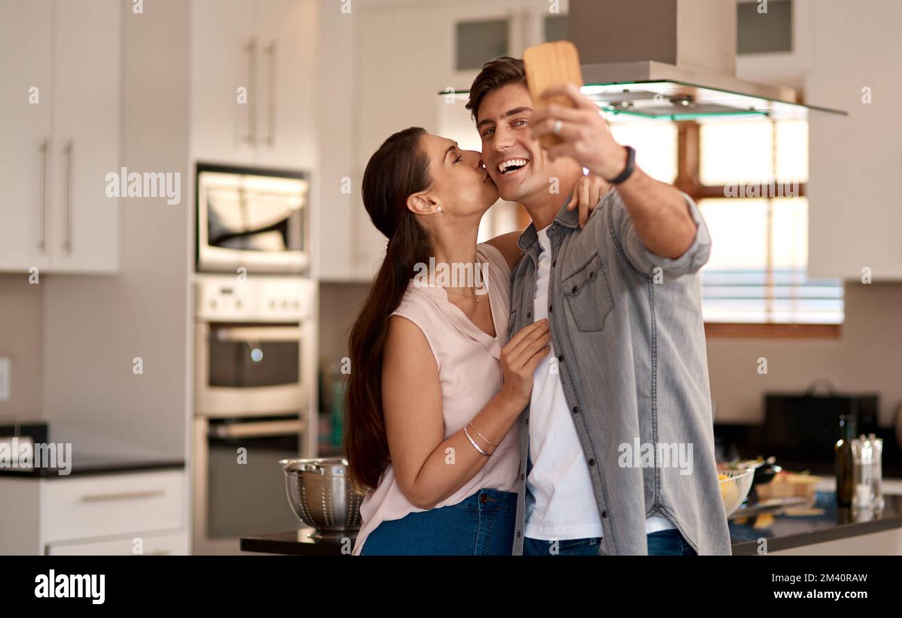 Jeder Moment mit dir sollte ein Selfie-Moment sein. Ein liebevolles Paar, das ein Selfie zusammen in der Küche zu Hause macht. Stockfoto