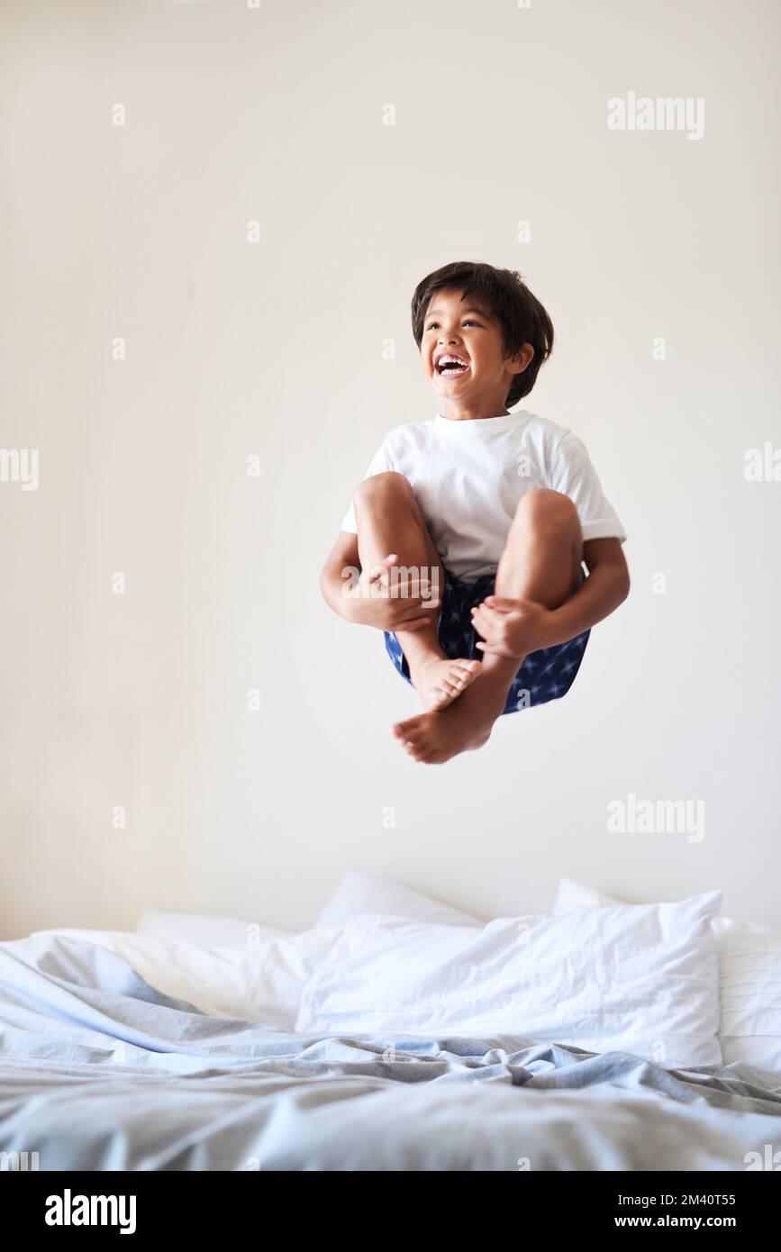 Eine Spritzbombe ist unterwegs. Aufnahme eines süßen kleinen Jungen, der zu Hause auf einem Bett spielt und springt. Stockfoto