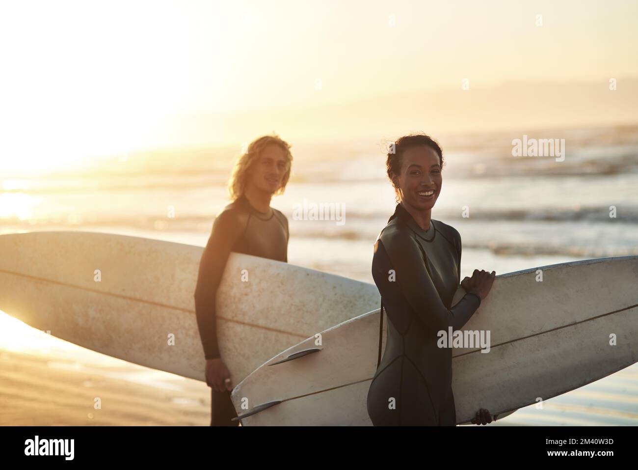 Du wirst uns finden, wo der Himmel auf das Land trifft. Ein fröhliches junges Paar, das am Strand surft. Stockfoto
