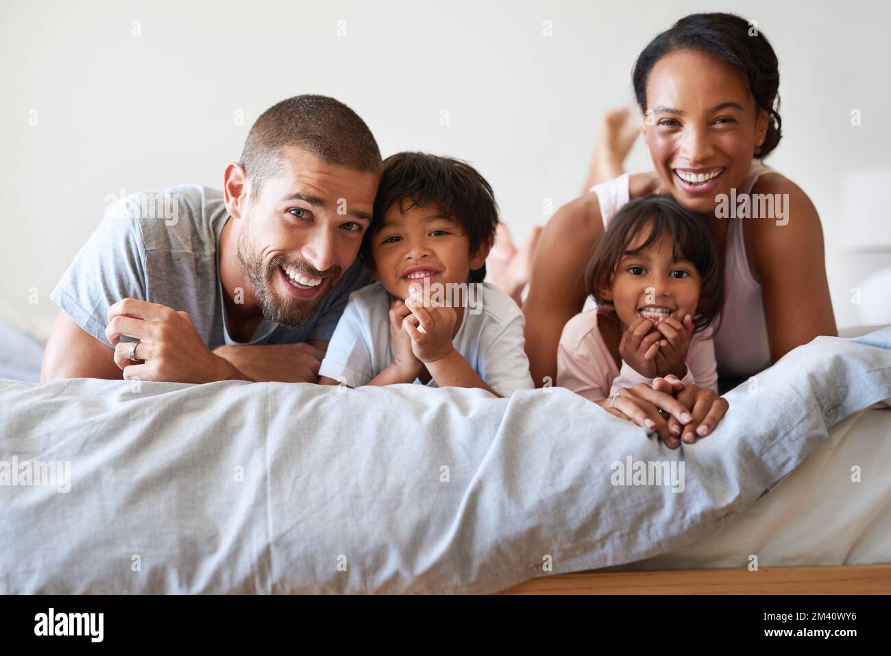 Unsere perfekte kleine Familie. Porträt einer wunderschönen, jungen vierköpfigen Familie, die sich zu Hause im Bett anfreundet und Zeit miteinander verbringt. Stockfoto