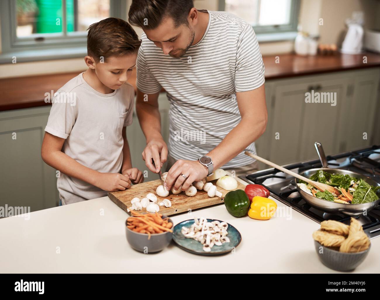 Pass nur auf, dass du dich nicht schneidest. Ein Junge, der seinem Vater beim Kochen hilft. Stockfoto